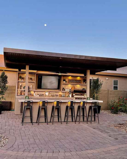 Outdoor kitchen with bar stools and a television under a clear blue sky.