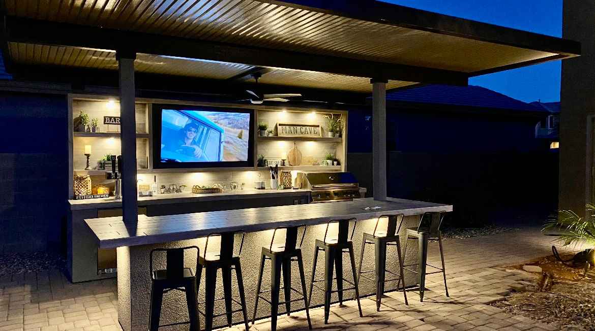 Outdoor kitchen with bar area and TV screen at night