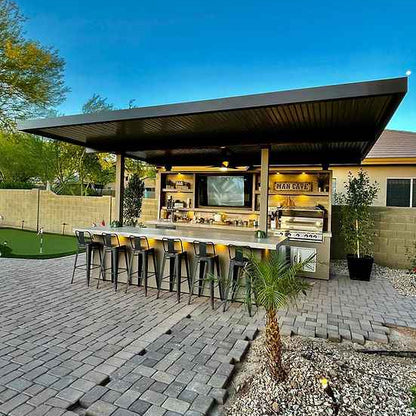 Outdoor kitchen with bar area on a patio, featuring a television and various appliances.